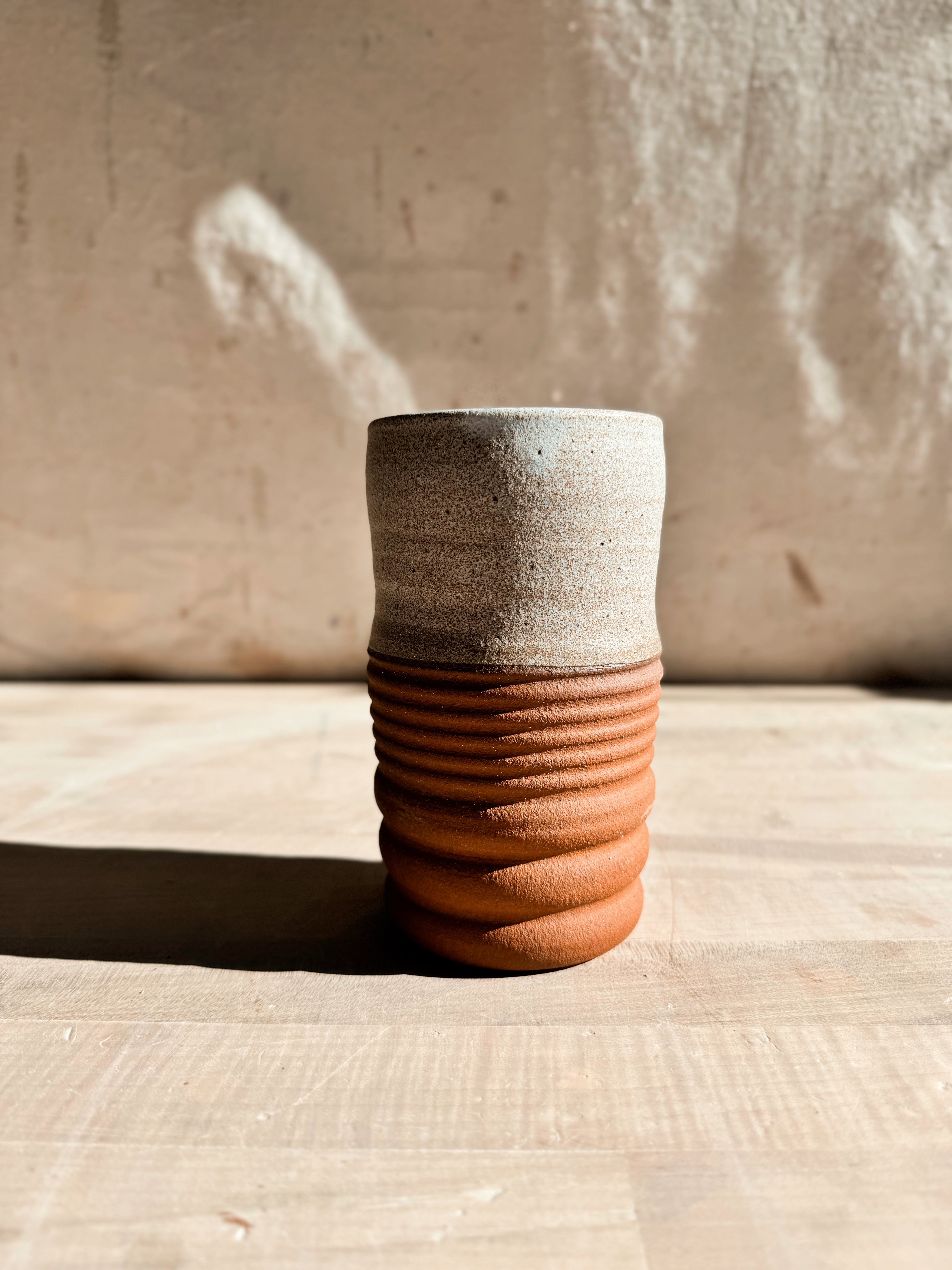 Textured Tumbler: close front view of a cup with speckled light glaze and a horizontally ridged raw clay base.