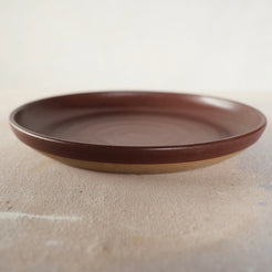 Country Rim Dinner Plate in reddish-brown glaze, resting flat on mottled studio canvas showing its raised outer lip.