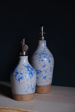 Wander Tall Oil Bottle standing behind a smaller matching cruet in white glaze with bold cobalt blue speckles.