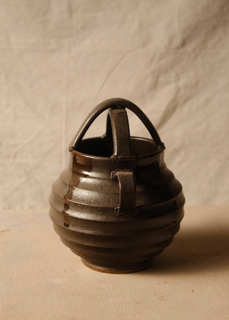 Regal glazed stoneware vase rotated to show one side loop handle, ribbed round body, and crossed top arch.