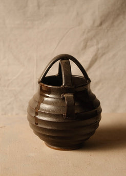 Regal glazed stoneware vase rotated to show one side loop handle, ribbed round body, and crossed top arch.