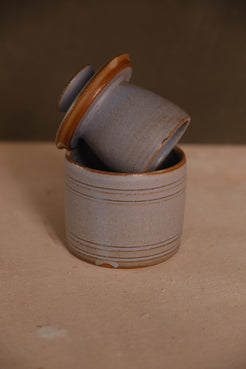 Butterbell keeper with carved grooves, bell lid angled on base, in a speckled pale blue glaze showing bare clay rim trims.