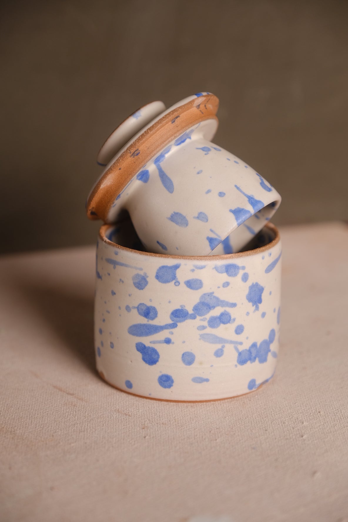 Butterbell ceramic keeper with blue splatter and flecks on white glaze, bell lid angled upside down within base rim.