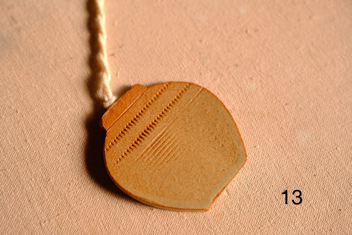 Ceramic ornament rounded jar cutout featuring stamped dash bands and fine horizontal line patterns, numbered thirteen.