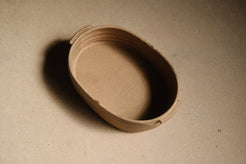 Maize Hot Dish empty and unglazed, raw sandy clay, oval interior and ribbed sides, small rim tabs, seen from above.