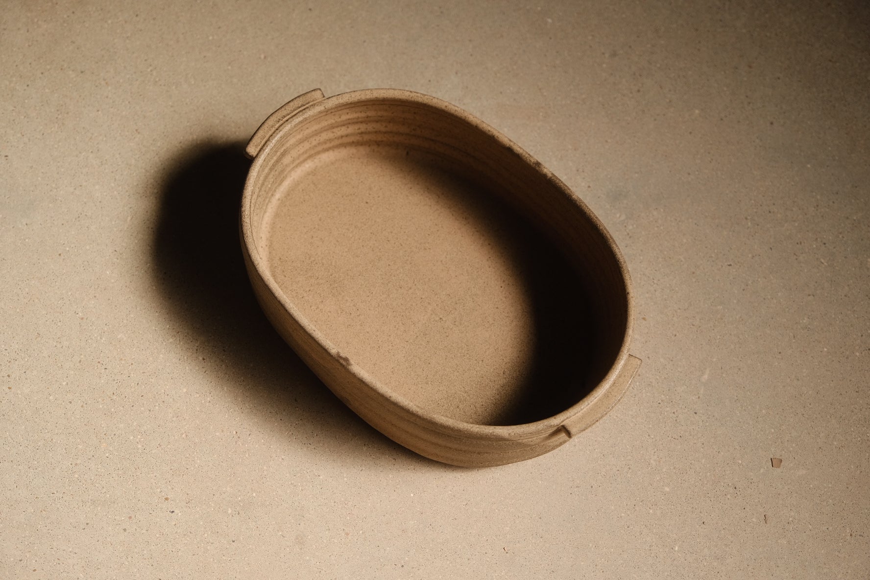 Maize Hot Dish empty and unglazed, raw sandy clay, oval interior and ribbed sides, small rim tabs, seen from above.