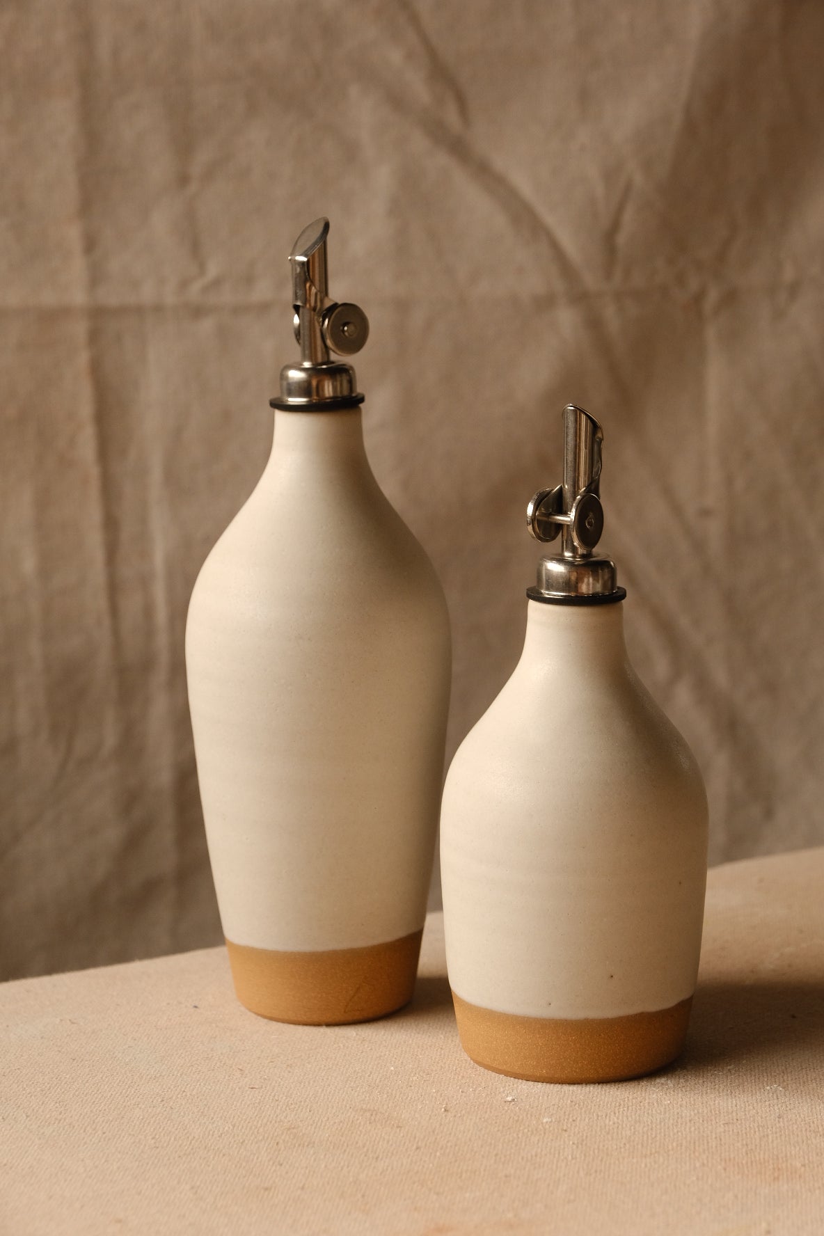 Wander Oil Bottle pair in off-white glaze, tall bottle forward and small bottle offset to the right.