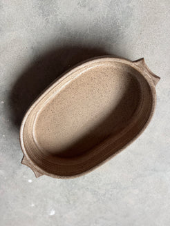 Speckle Maize Hot Dish, top-down view of the oval ceramic baker with side tab handles on concrete.
