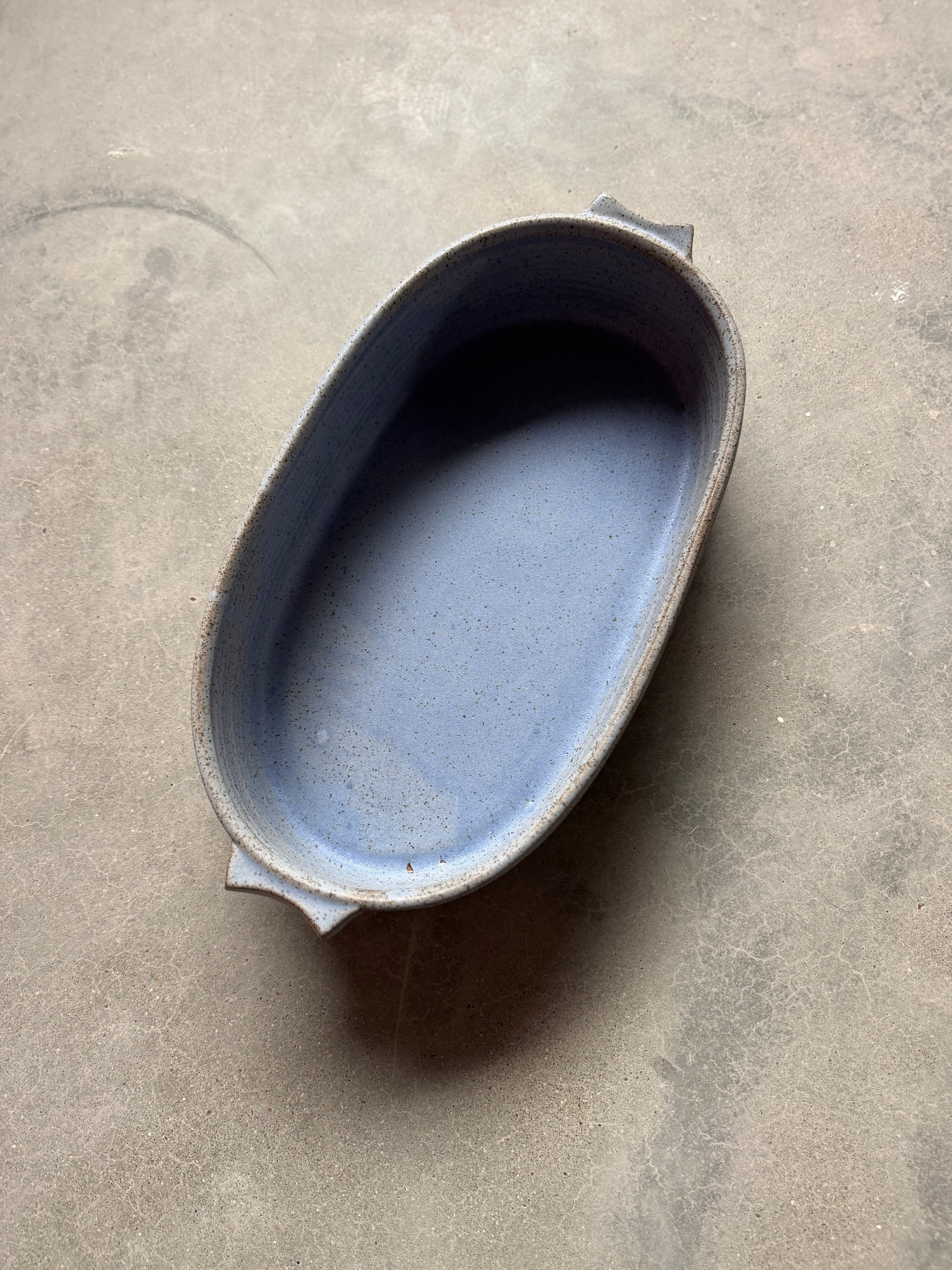 Speckle Cenote Hot Dish, oval ceramic casserole baker with side tab handles seen from above on a concrete surface.