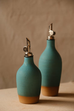 Wander Oil Bottle pair in matte teal glaze, small bottle forward with raw clay foot on canvas.