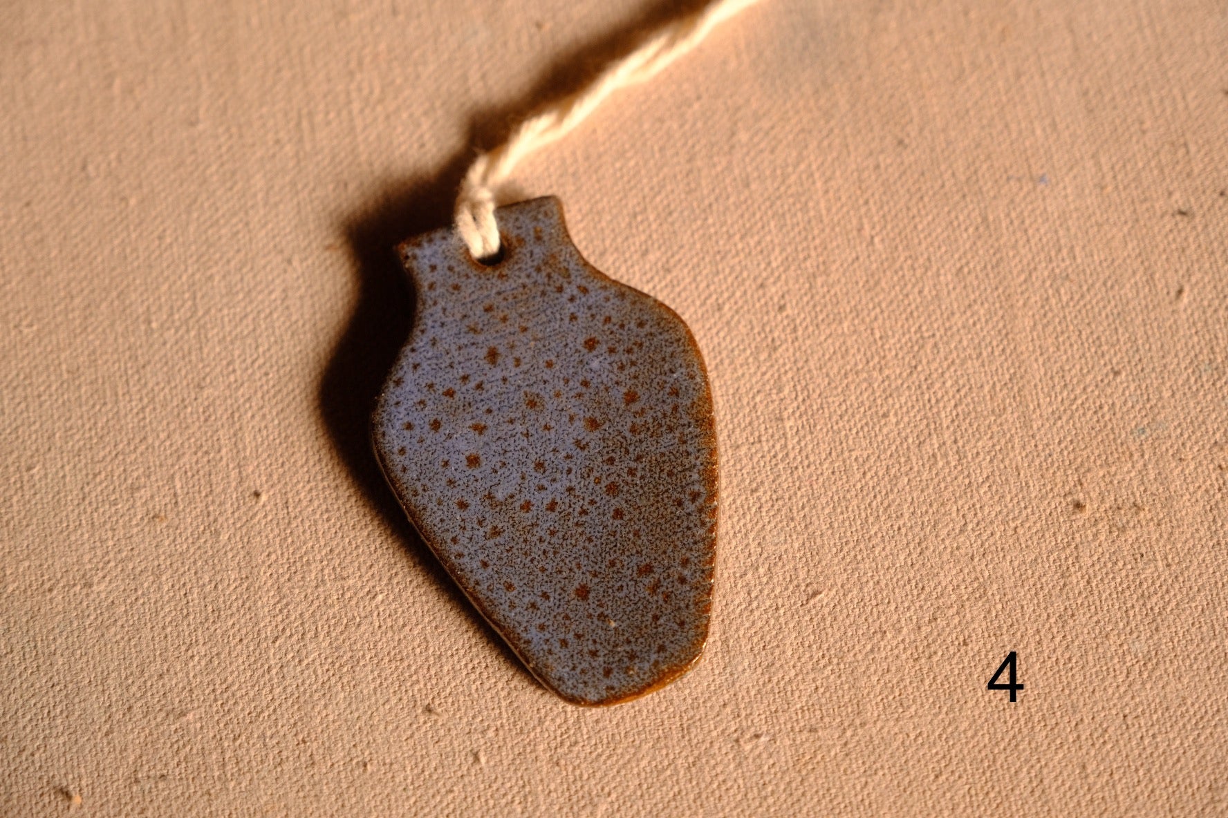 Ceramic ornament tapered vase cutout with dense blue and tan speckles and a hanging string, numbered four on fabric.