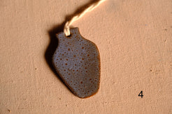 Ceramic ornament tapered vase cutout with dense blue and tan speckles and a hanging string, numbered four on fabric.