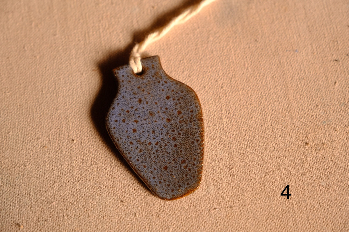 Ceramic ornament tapered vase cutout with dense blue and tan speckles and a hanging string, numbered four on fabric.