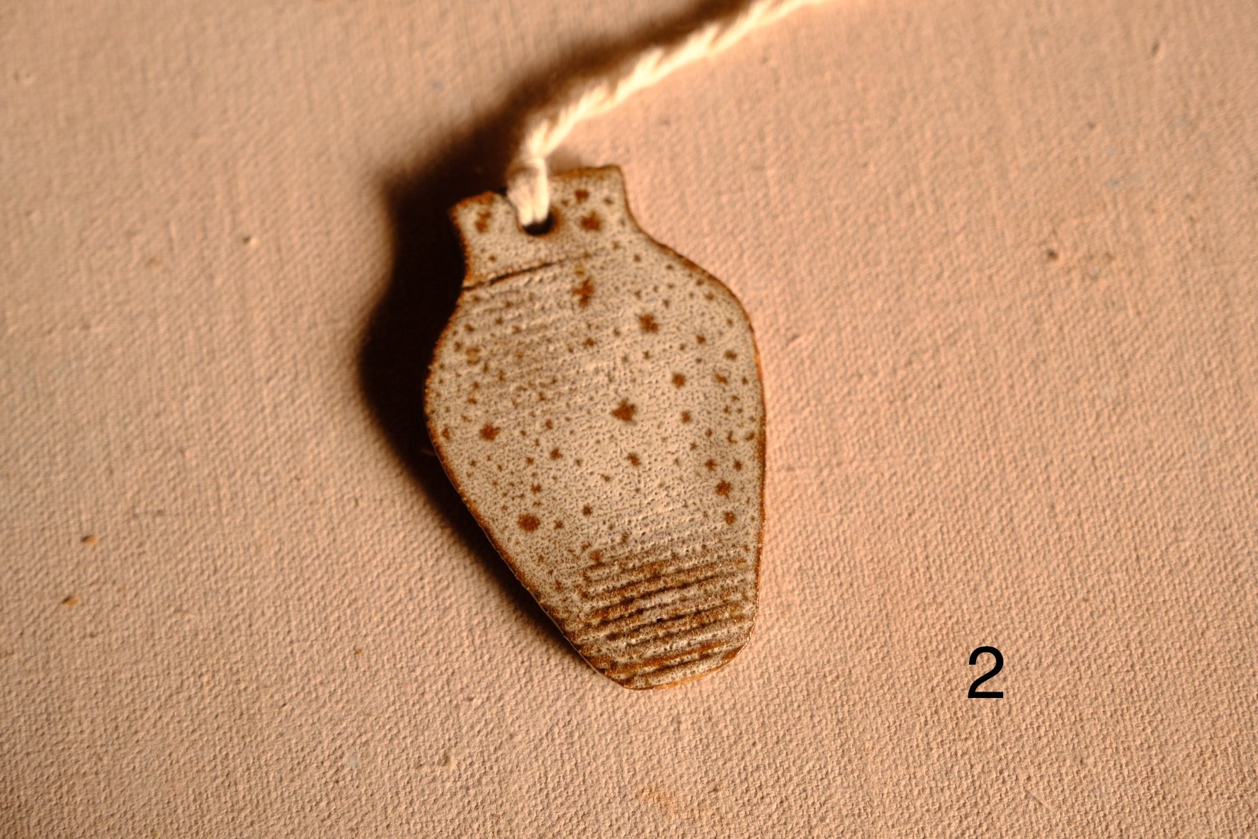 Ceramic ornament tapered vase shape with speckled oatmeal glaze and carved bands near the bottom, numbered two.