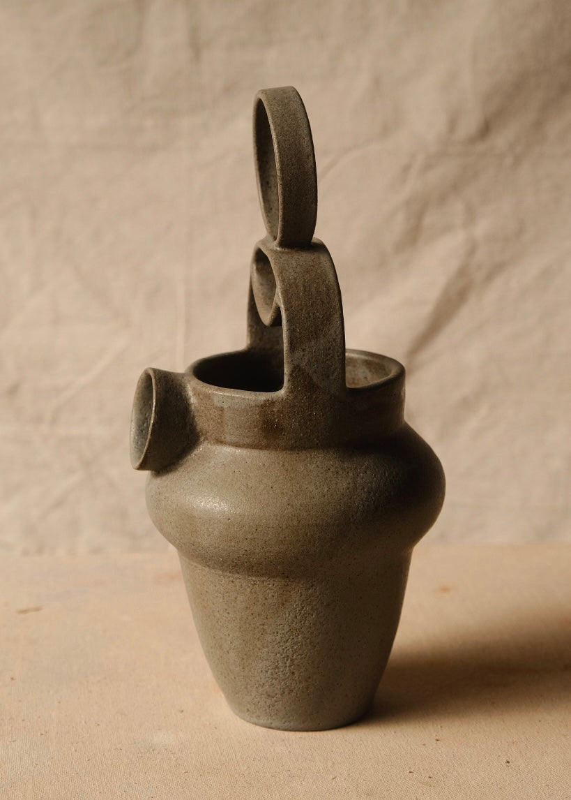 Rising Moon stoneware pitcher angled to the left, showing its side profile, arched geometric handle, and cylindrical spout.