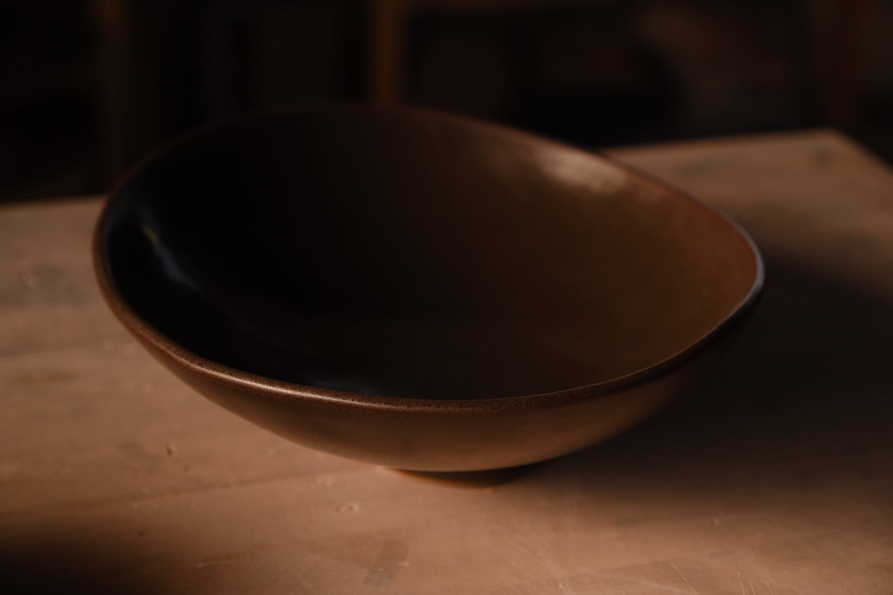 Wander Footed Oval Server in dark bronze glaze, viewed from the side on a wood surface in warm studio lighting.