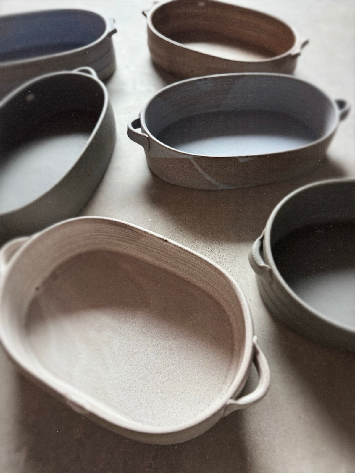 Speckle Storm Hot Dish among six oval ceramic baking dishes in assorted glazes arranged across a flat work surface.