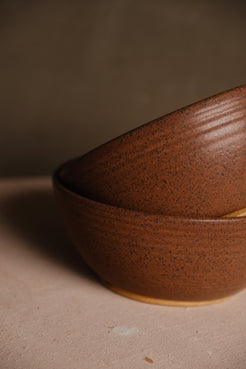 Speckled Buff Ramen Bowl stacked inside another at an angle on fabric, close-up on exterior glaze