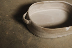 Blanca Hot Dish, close low three-quarter angle focused on the looped side handle, interior ridges, and speckled clay rim.