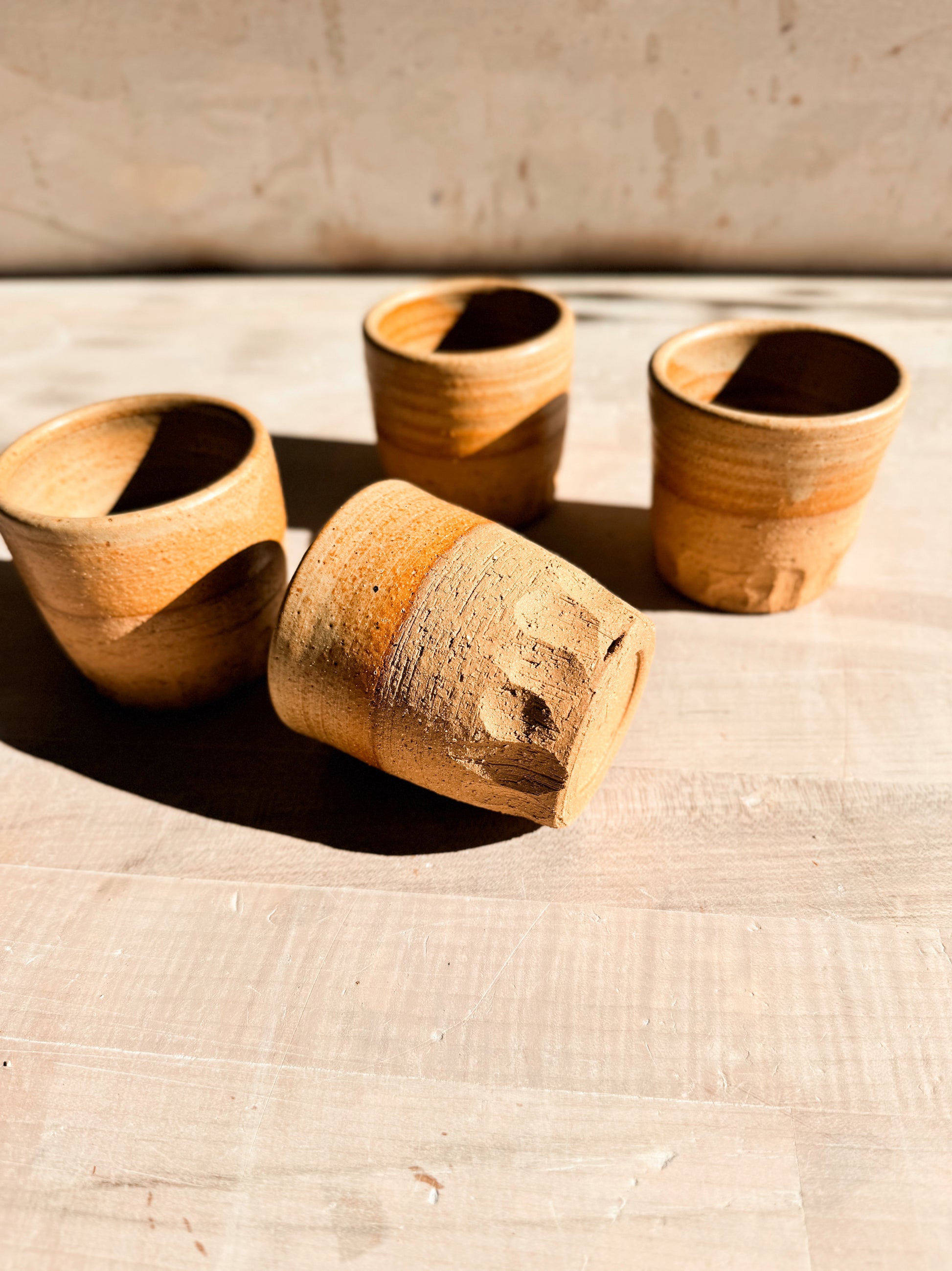 Aura Sipper cups, one stoneware tumbler tilted on its textured side in front of three upright matching cups on wood.