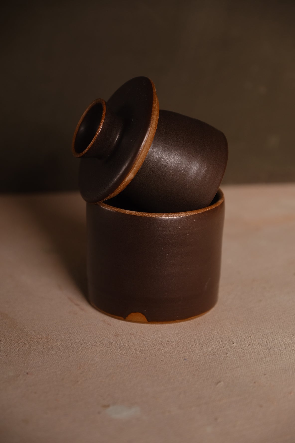 Butterbell crock with inverted bell lid resting angled on rim, dark brown satin glaze and bare clay rim edges.
