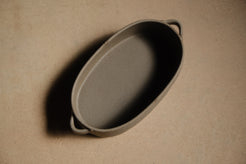 Storm Hot Dish: high overhead angle looking down into the empty oval baker with two side loop handles on a tan surface.