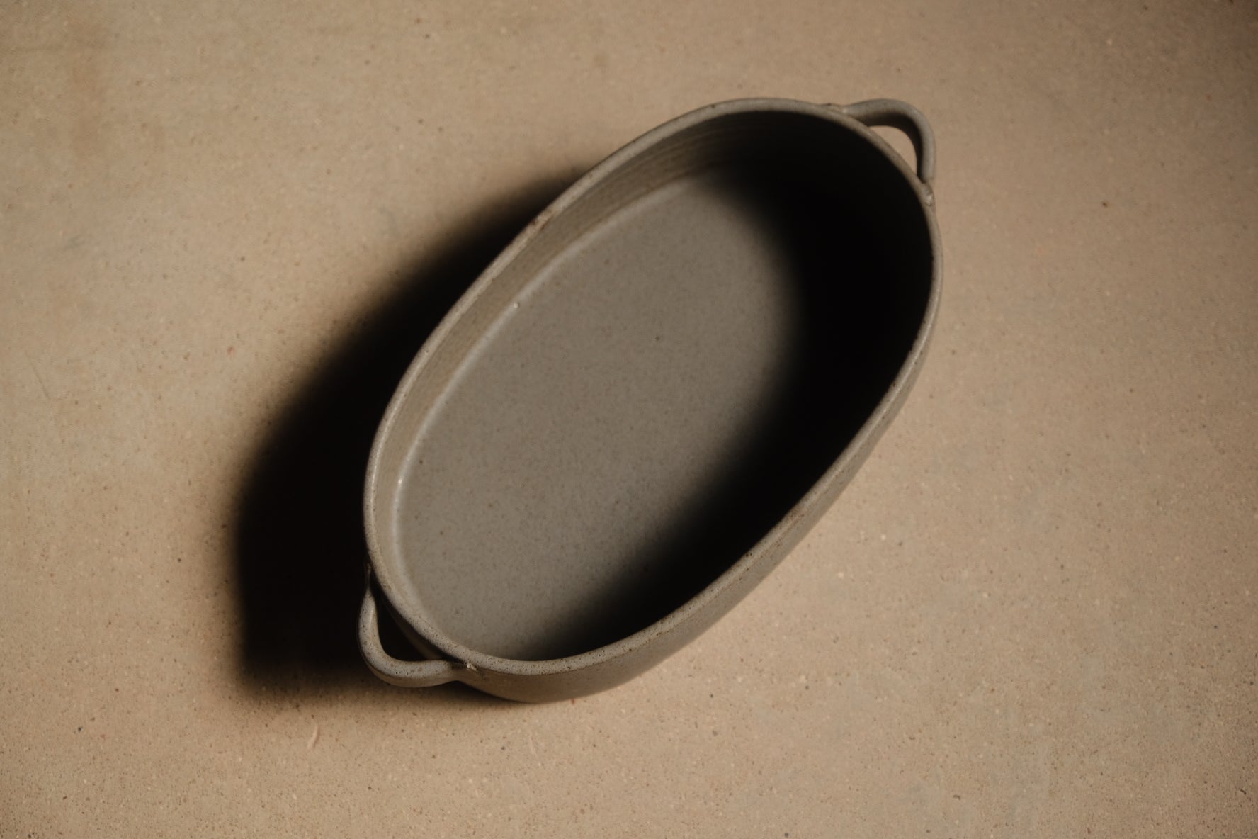 Storm Hot Dish: high overhead angle looking down into the empty oval baker with two side loop handles on a tan surface.