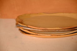 Tera Platter, side angle of a stack of platters showing wavy rims and bare clay edges.