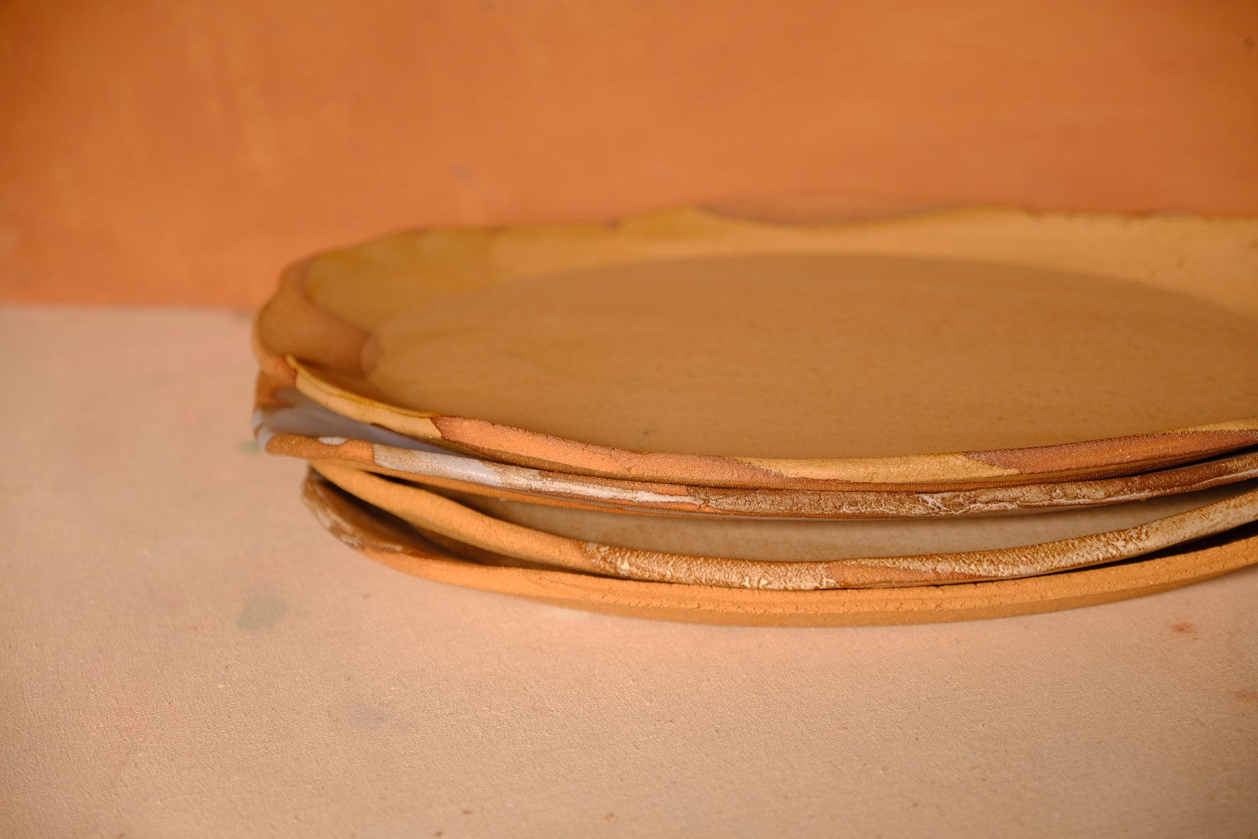 Tera Platter, side angle of a stack of platters showing wavy rims and bare clay edges.