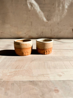 Aura Sipper cups, a pair of short ceramic tumblers side by side on wood, showing glazed rims and carved lower bases.