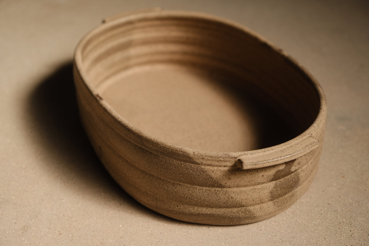 Maize Hot Dish at a three-quarter angle, unglazed sandy clay, ribbed outer wall and smooth interior basin.