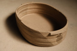Maize Hot Dish at a three-quarter angle, unglazed sandy clay, ribbed outer wall and smooth interior basin.