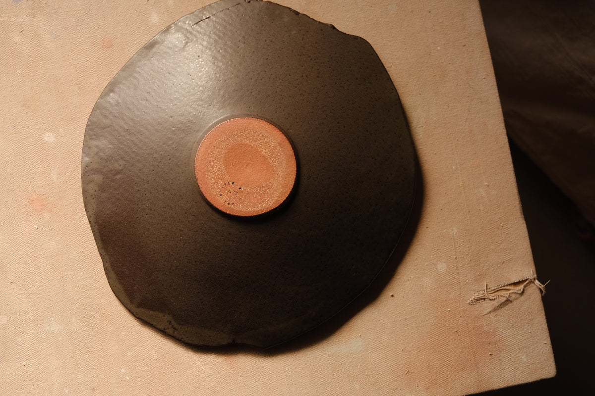 Mesa Platter base viewed from above, displaying the terracotta-toned round foot against a dark satin underside.