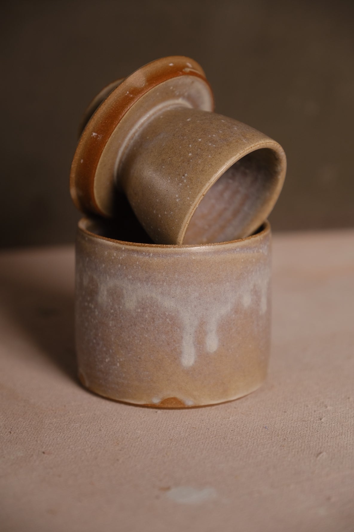 Butterbell with dripping white glaze over a speckled tan ground, bell lid tilted inside the base showing raw clay edges.