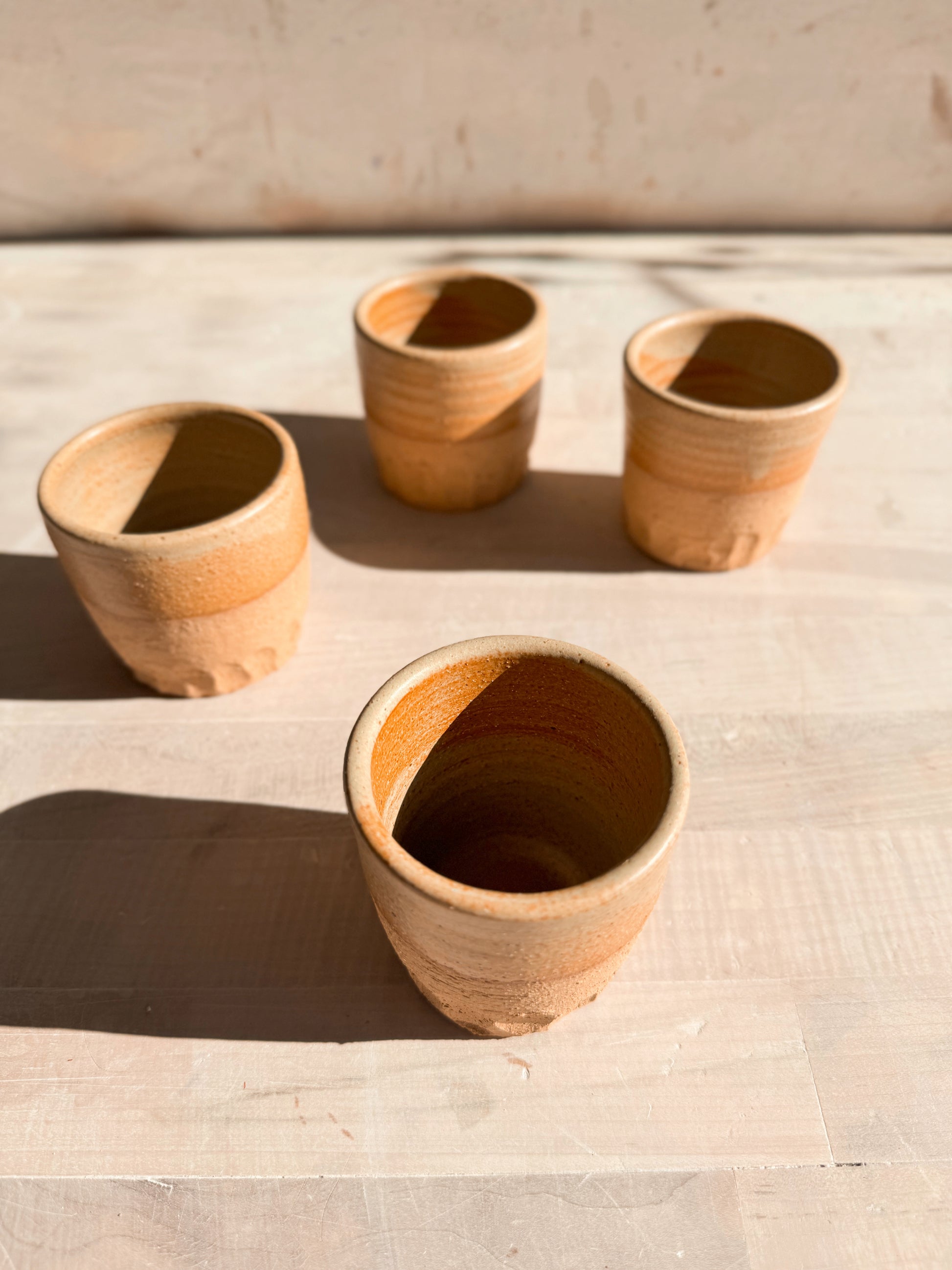 Aura Sipper cups, high-angle view focused on an open stoneware cup in the foreground with three cups spaced behind.