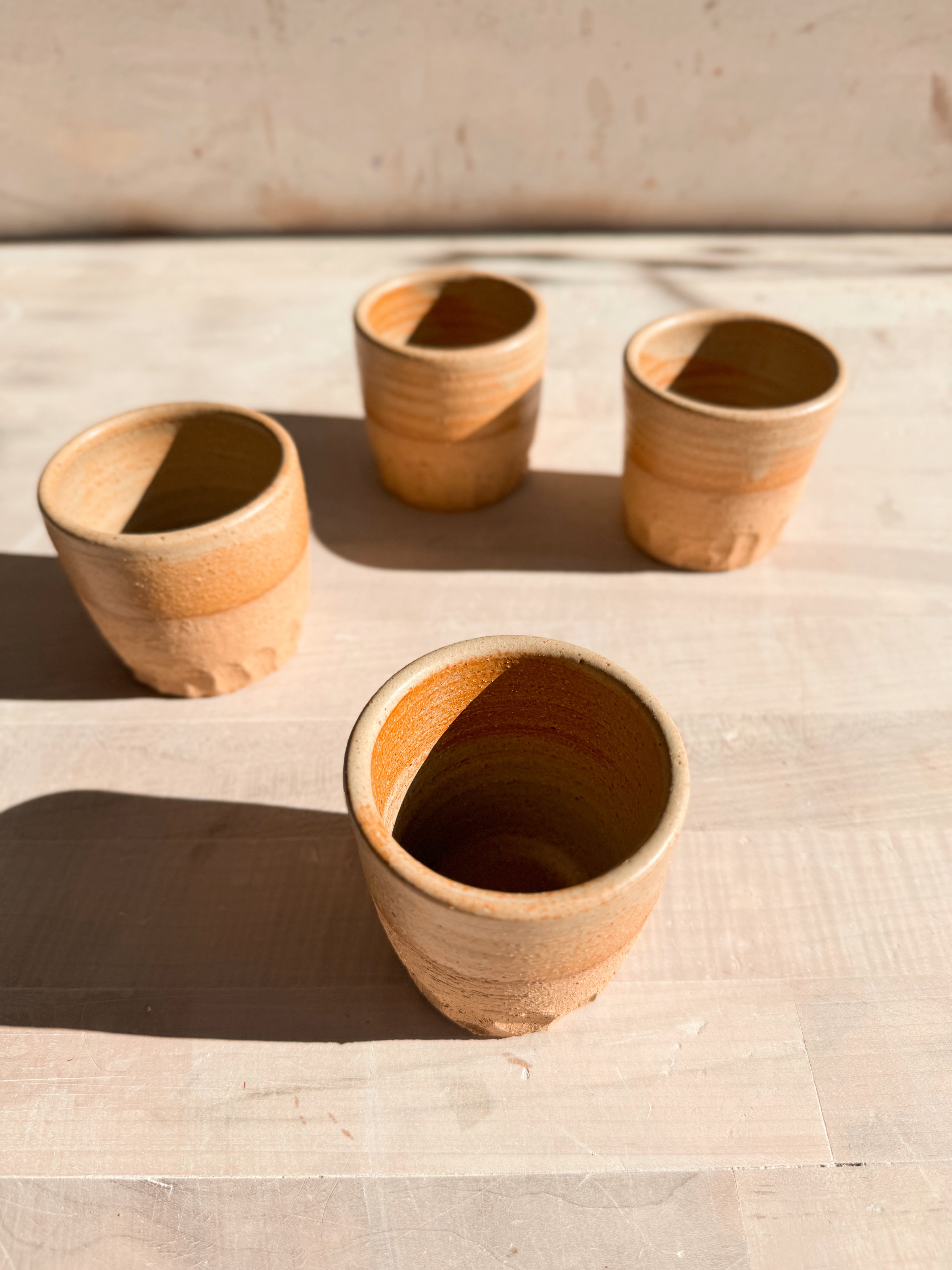 Aura Sipper cups, high-angle view focused on an open stoneware cup in the foreground with three cups spaced behind.
