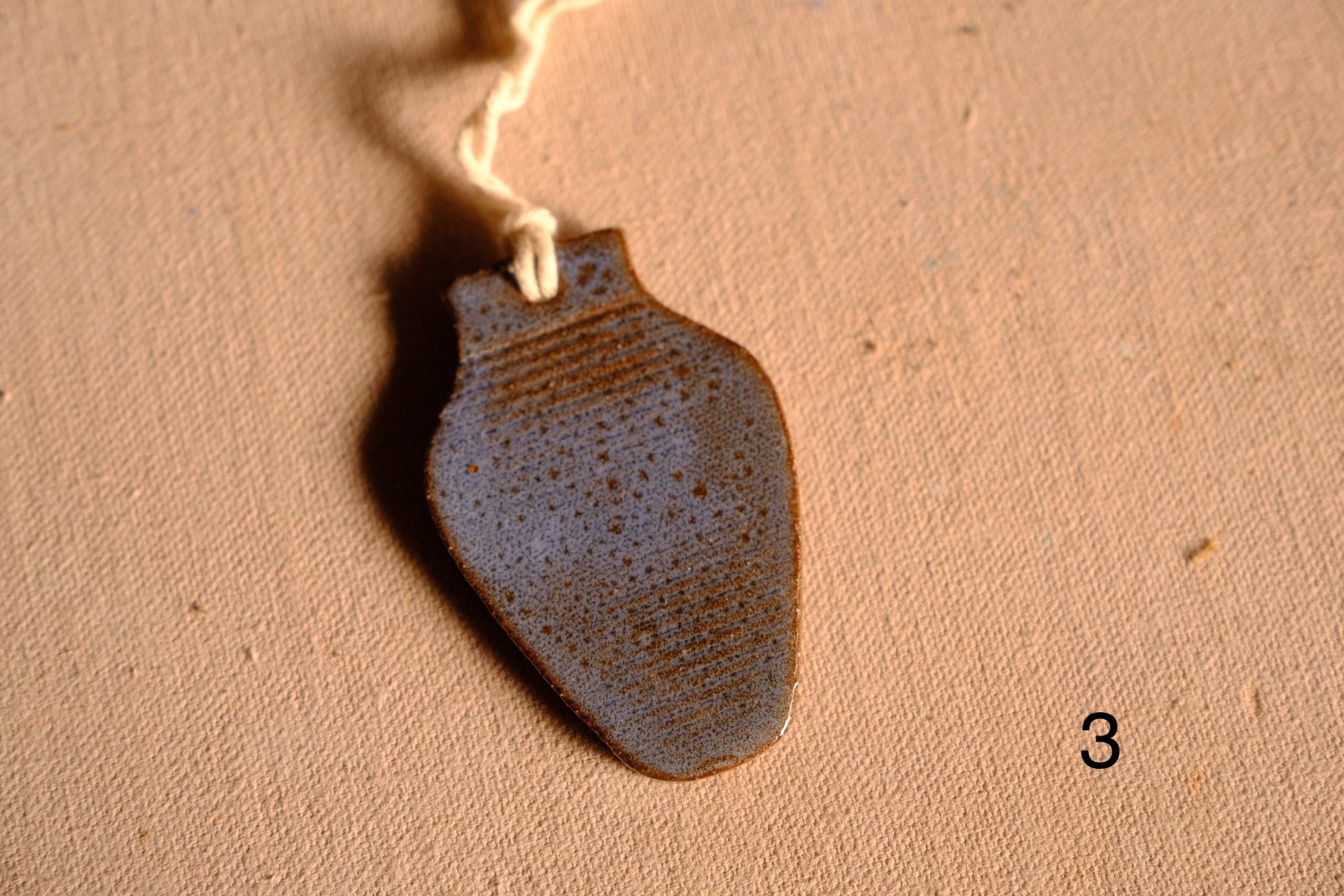 Ceramic ornament vase silhouette featuring a mottled blue and brown speckled glaze with hanging string, numbered three.