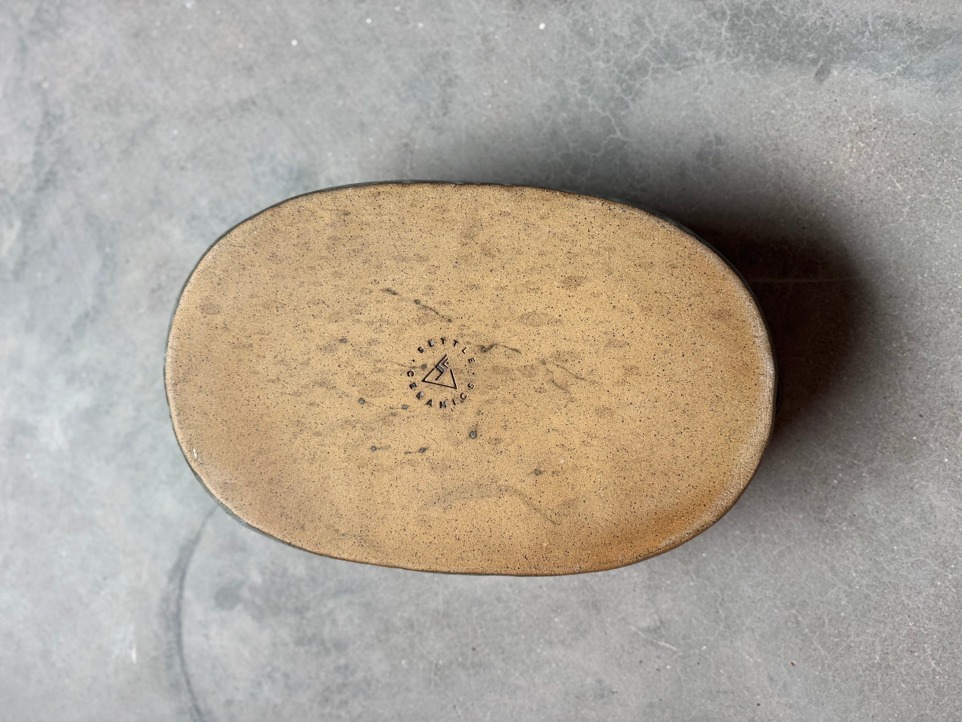 Speckle Storm Hot Dish, unglazed flat bottom showing raw tan clay stamped with the maker maker's maker mark logo.
