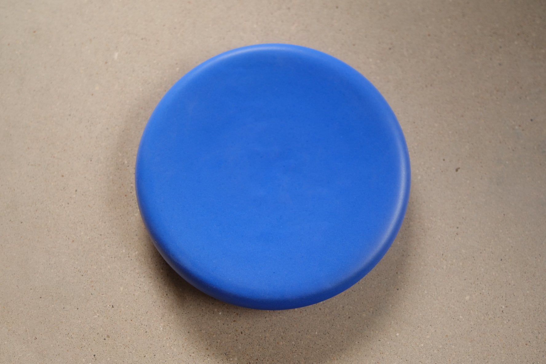 Bubble Plate viewed from above on concrete, showing a puffed, rounded matte blue dome shape.