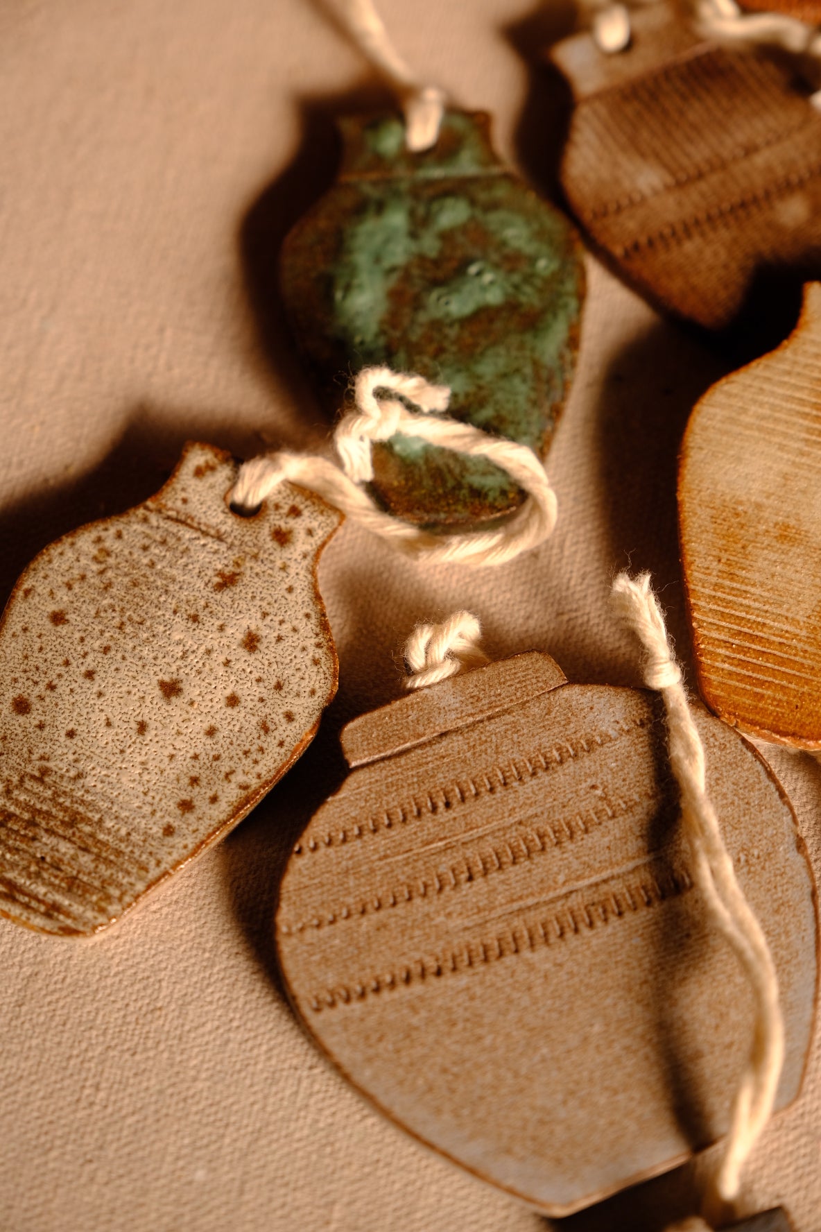 Ceramic ornaments in vase shapes showing speckled, green, and impressed line surfaces arranged together on fabric.