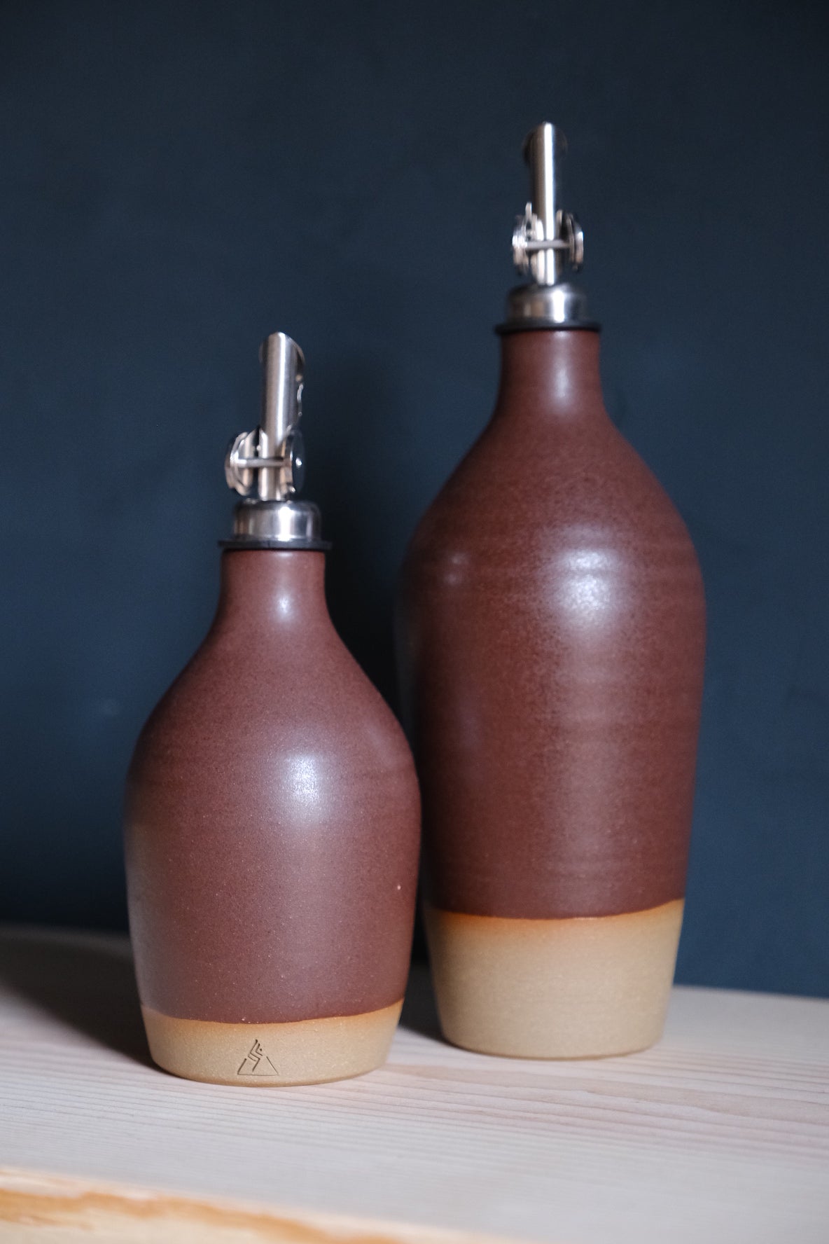Wander Oil Bottle pair in deep umber satin glaze, small bottle in front showing a stamped clay foot.