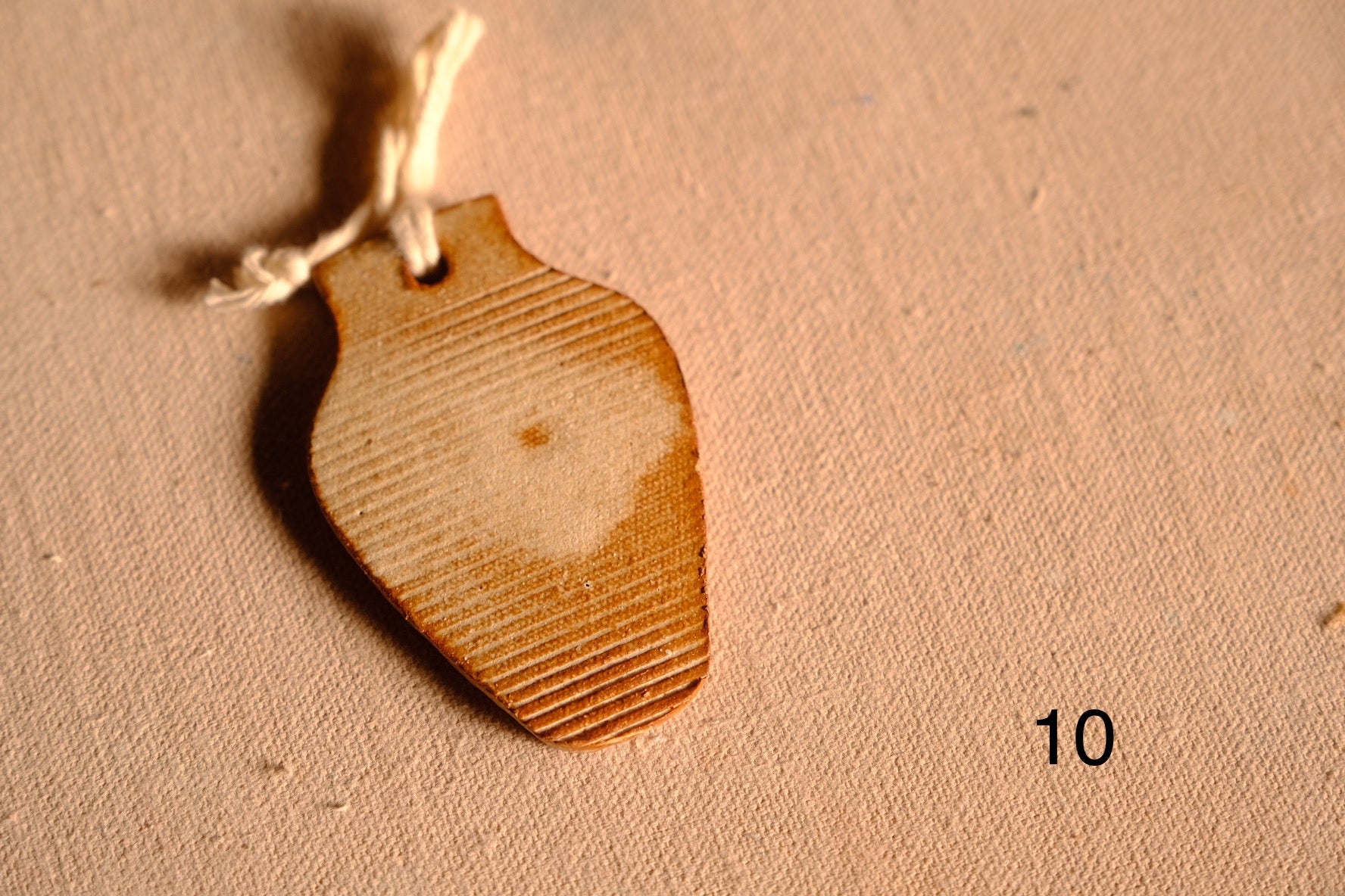 Ceramic ornament tapered vase cutout with fine horizontal ribbed lines across the clay surface, numbered ten.