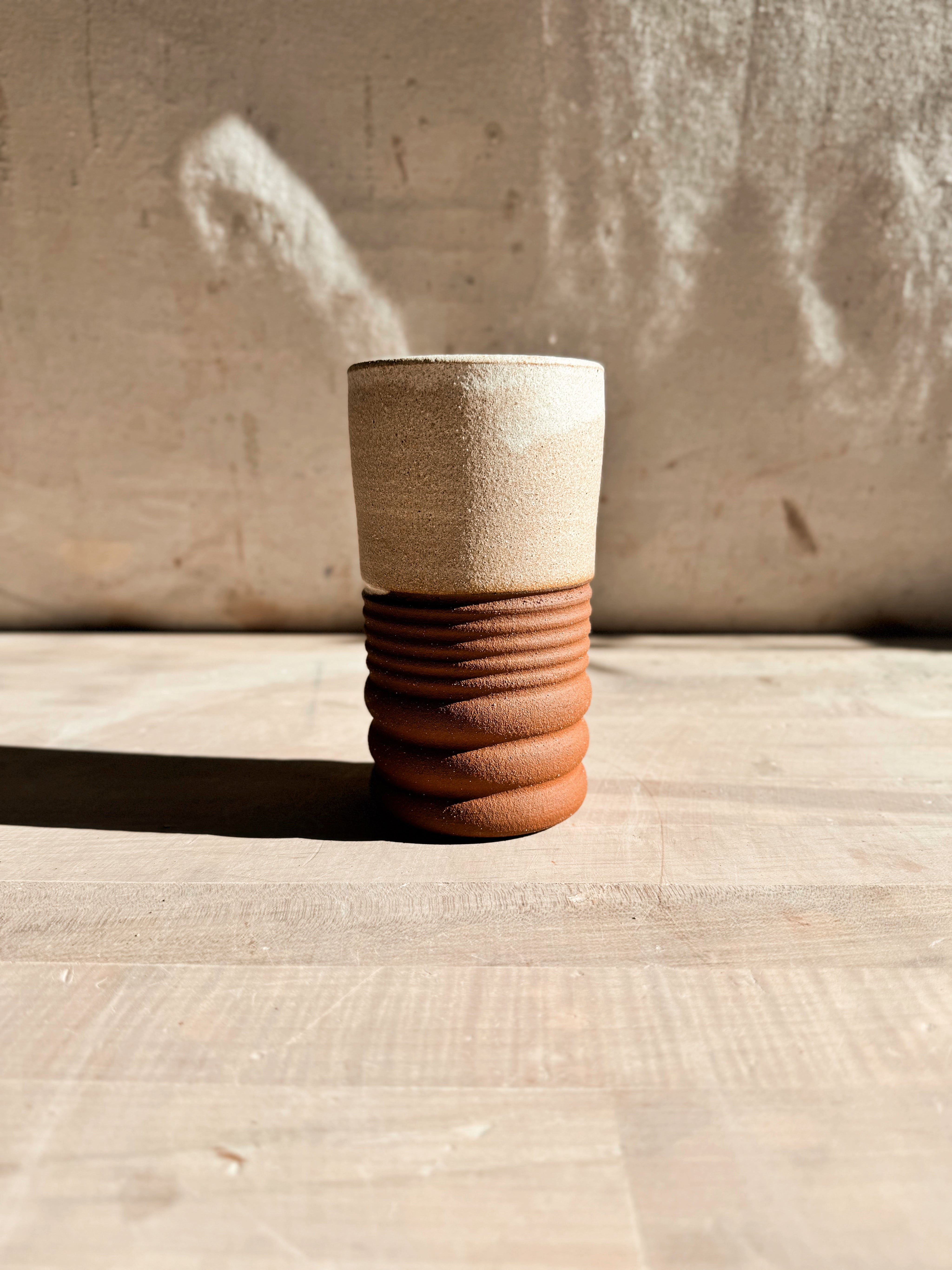Textured Tumbler: slender cup with a pale cream glazed upper section and ribbed raw clay base on a wood surface.