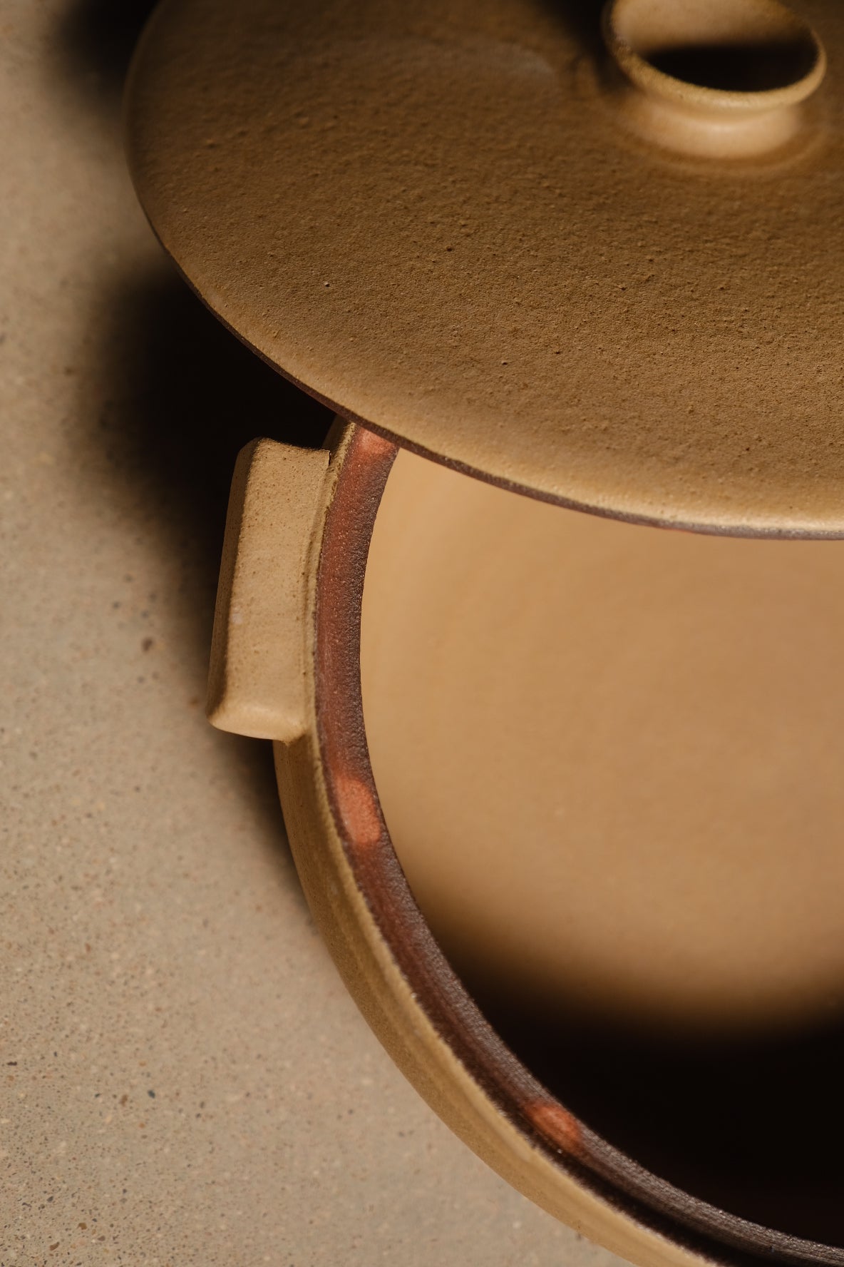Satin Sand Lidded Hot Dish detail: tab handle, exposed raw clay seam at the lid line, glazed amber interior.