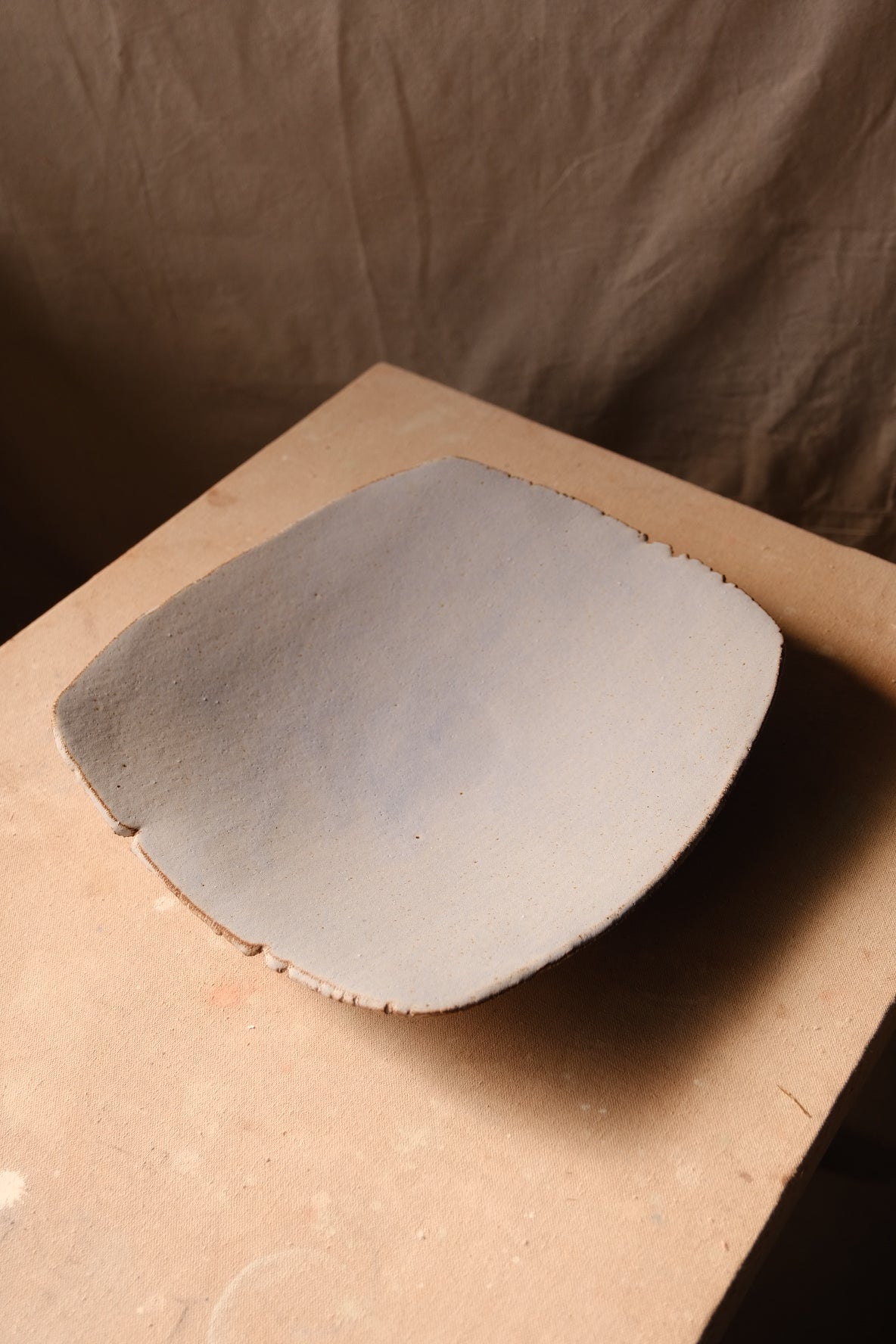 Mesa Platter with matte pale glaze, angled side view resting on a studio board with a slight rim curve.