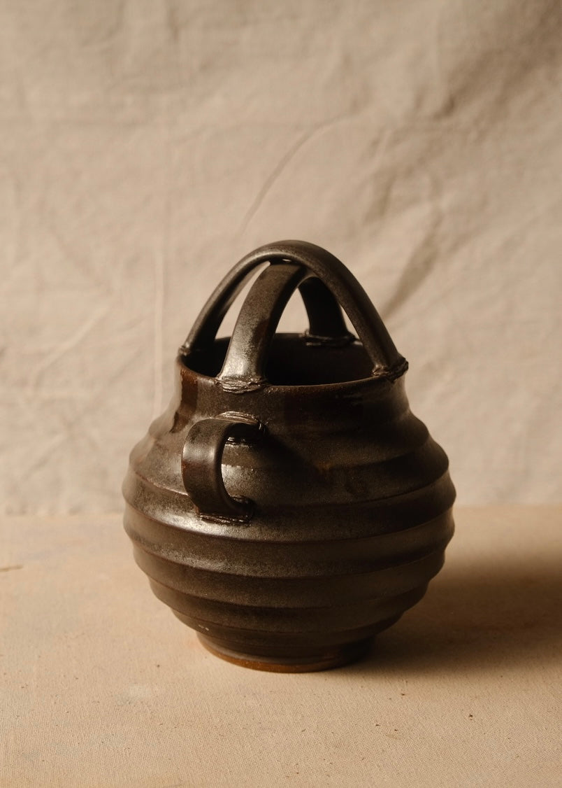Regal stoneware vase viewed side-on, highlighting a curved strap handle and horizontally ribbed body.