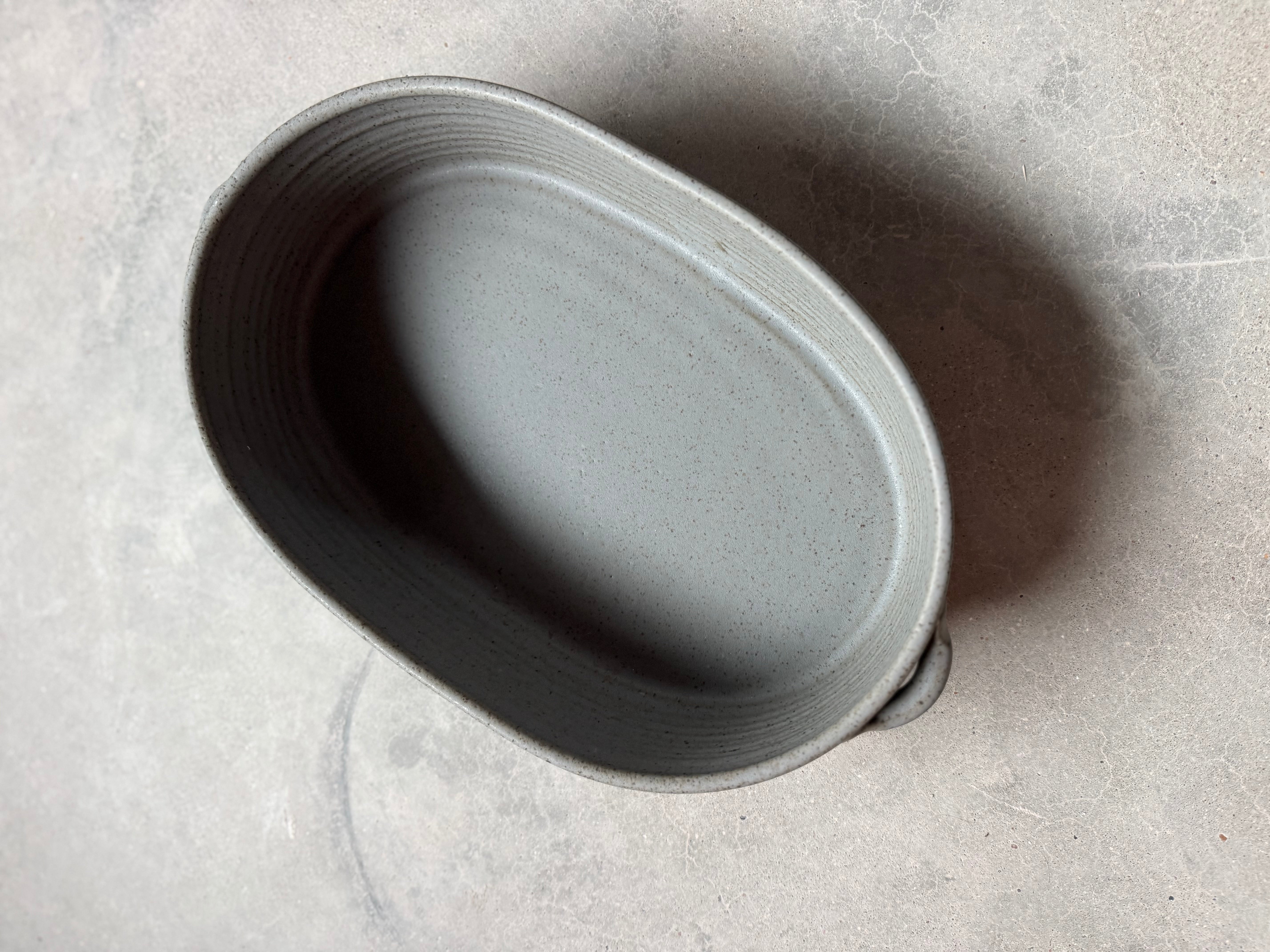 Speckle Storm Hot Dish, high-angle view looking inside the empty oval ceramic baker with side loop handles on concrete.