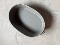 Speckle Storm Hot Dish, high-angle view looking inside the empty oval ceramic baker with side loop handles on concrete.