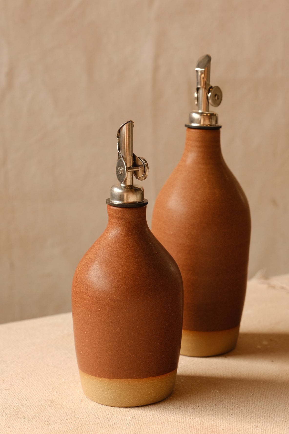 Wander Tall Oil Bottle beside a small matching cruet in warm rust brown matte glaze over bare clay feet.