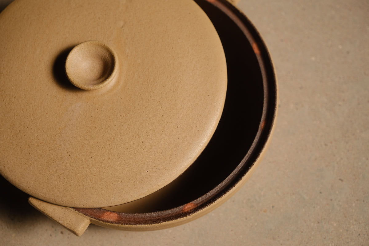 Satin Sand Lidded Hot Dish angled overhead shot with lid shifted aside to show inner rim seat and interior cavity.